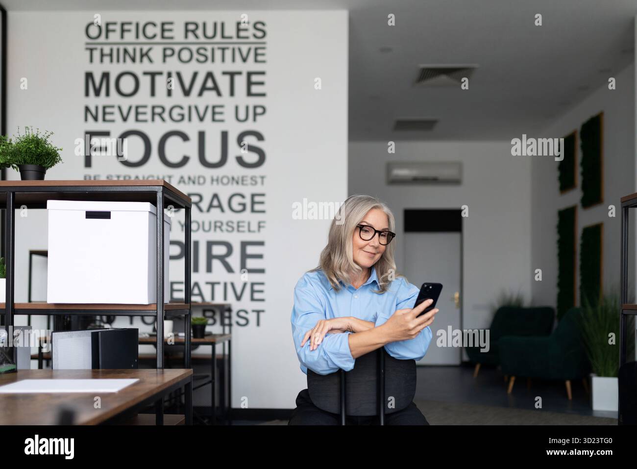 Femme d'affaires autonome et confiante tenant un téléphone dans ses mains au bureau Banque D'Images