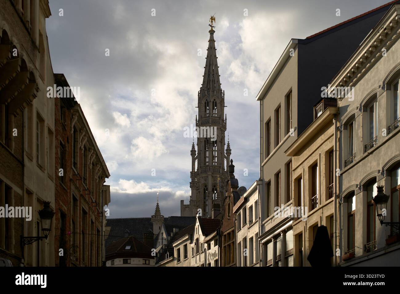 Une rue européenne étroite avec des bâtiments historiques et une grande tour d'église ornée sous un ciel nuageux. Bruxelles, Belgique Banque D'Images