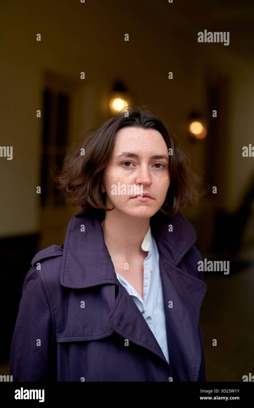 Jeune femme avec les cheveux bruns courts dans le manteau violet regarde dans la caméra dans le couloir sombre. Bruxelles, Belgique Banque D'Images