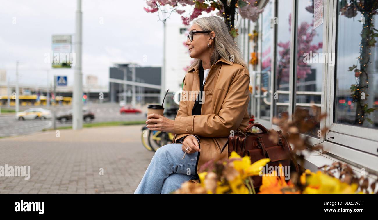 Femme forte de cinquante ans buvant du café tout en étant assise dans la ville Banque D'Images