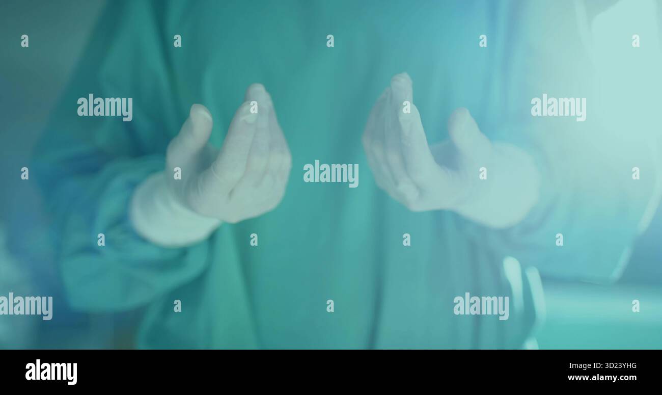 Chirurgien tenant les mains stériles gantées au niveau de la poitrine dans la salle d'opération avec des gommages verts Banque D'Images