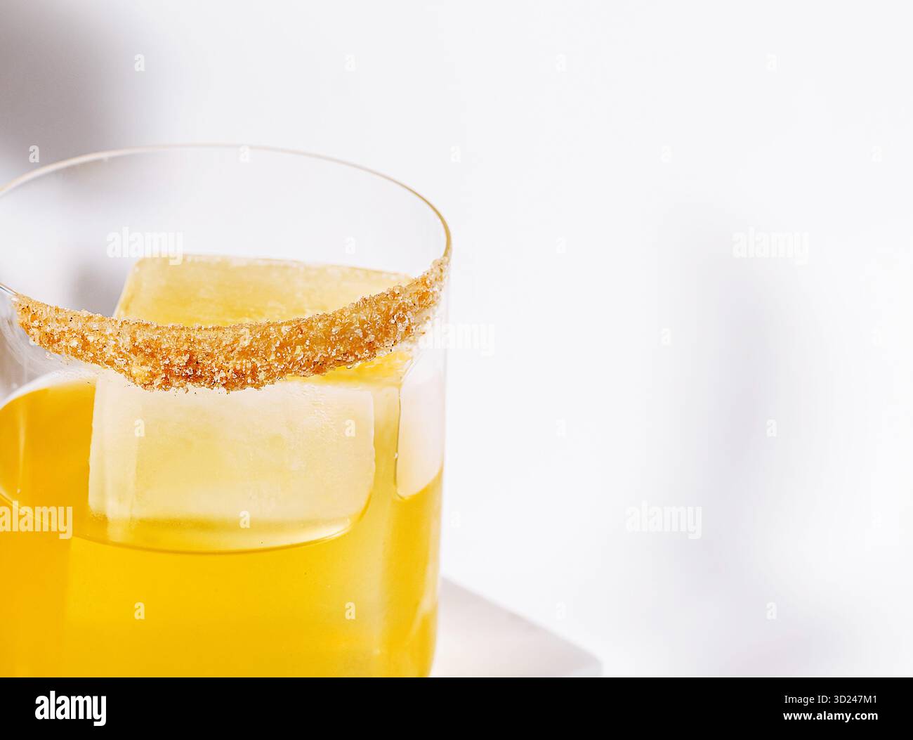 Cocktail jaune vif avec bordure de sucre et glace assis sur une surface blanche Banque D'Images