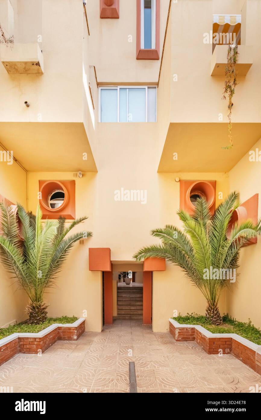 Détail de façade d'un immeuble d'appartements moderne avec un style géométrique jaune et terre cuite, avec deux palmiers dans la cour Banque D'Images