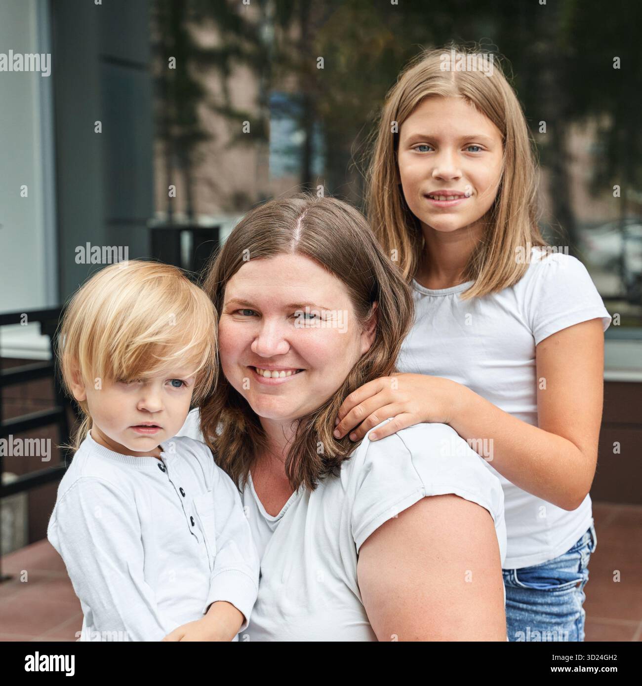 Femme adulte caucasienne avec des enfants caucasiens souriant à l'extérieur en blanc décontracté Banque D'Images