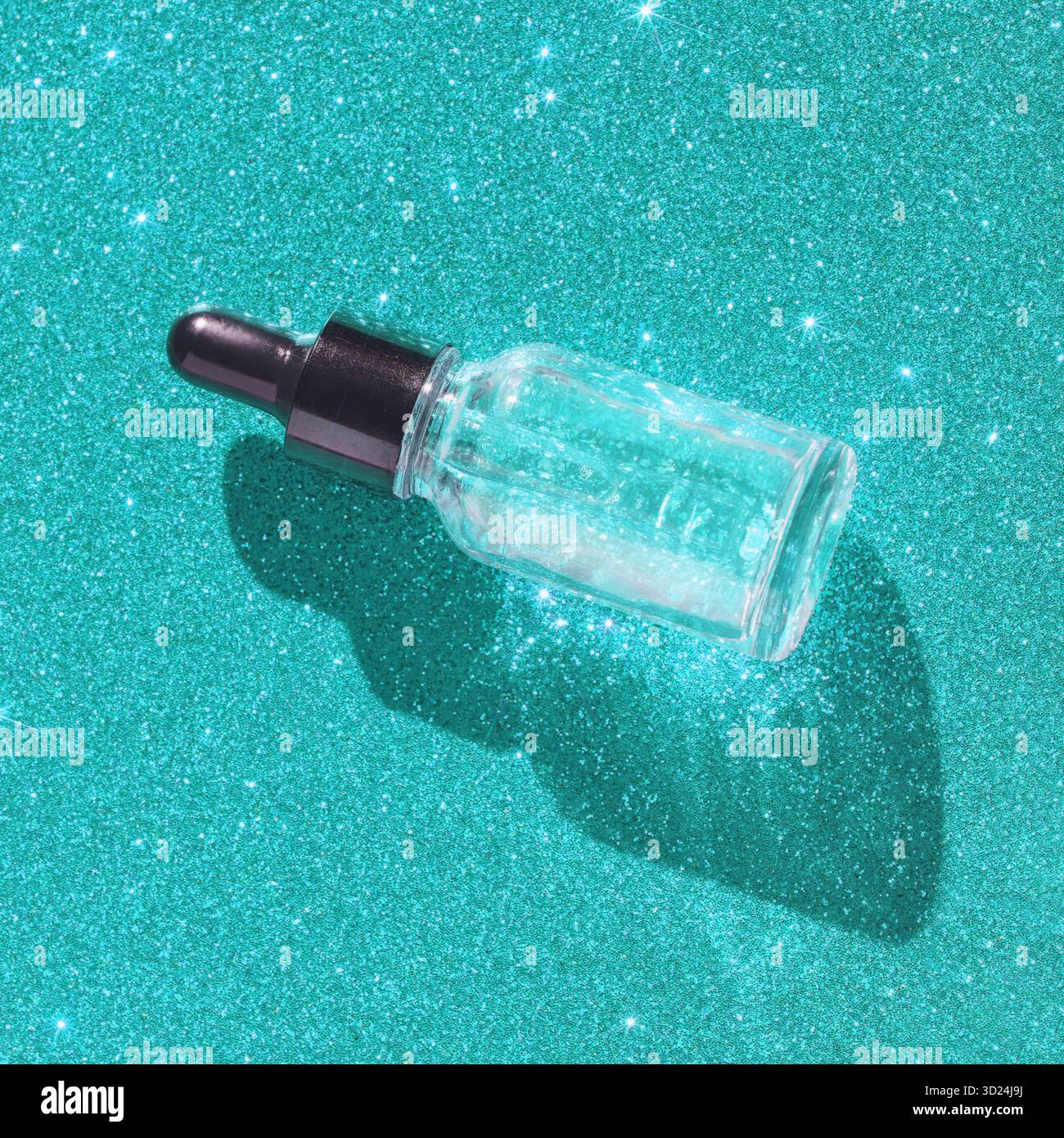 Bouteille compte-gouttes en verre sur surface turquoise pailletée avec des ombres étincelantes Banque D'Images