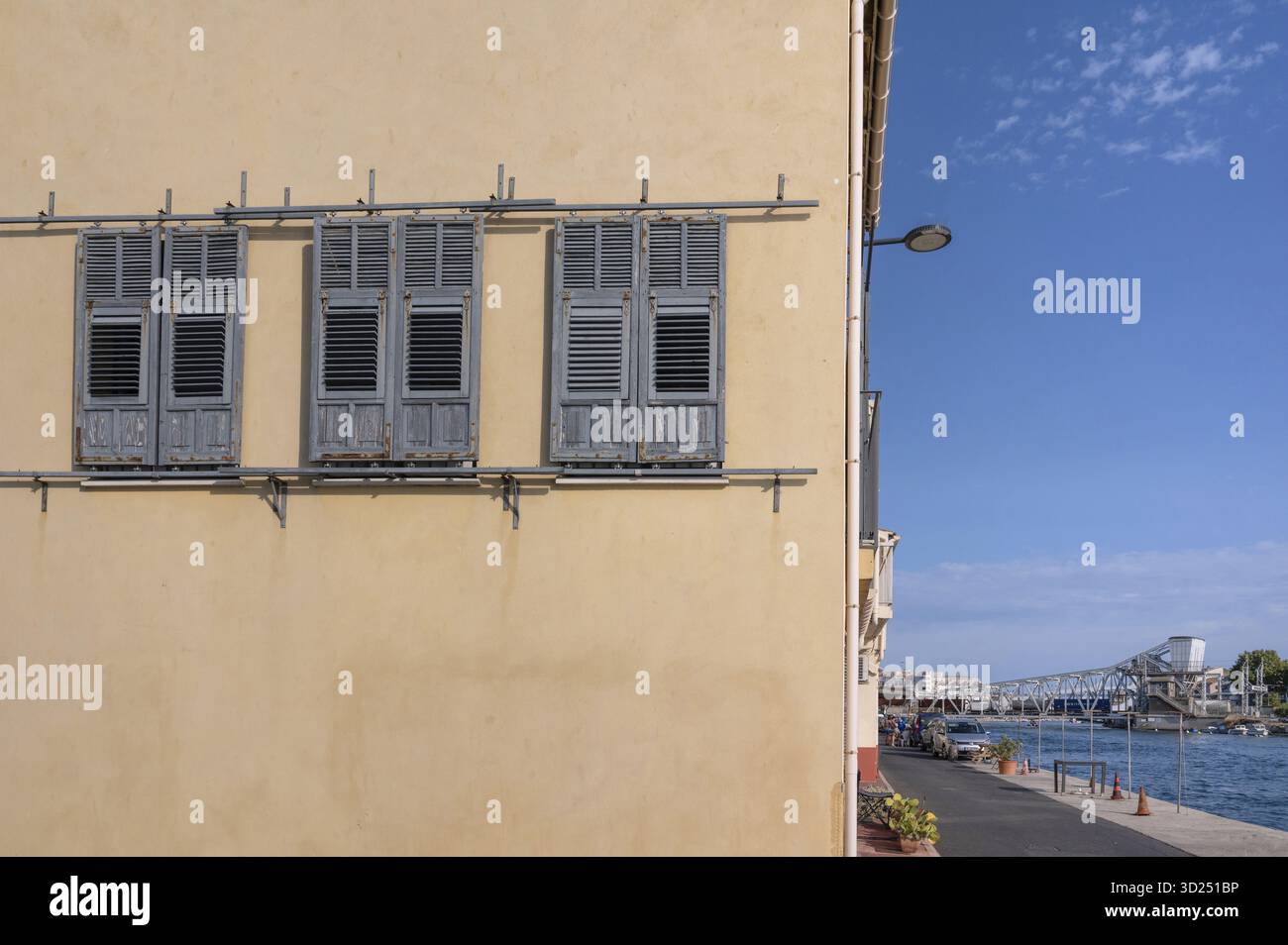 Façade de maison jaune avec trois volets en bois gris à déplacer et une vue sur le canal de Sète (anciennement canal Royal) aux virages en acier distinctifs Banque D'Images