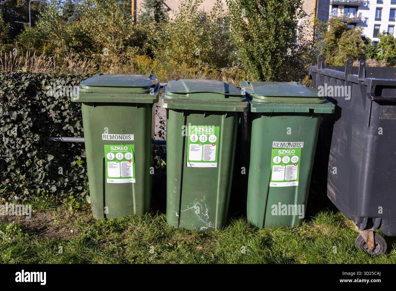 Poznan, Pologne - 24 septembre 2025 : trois bacs de recyclage verts REMONDIS pour le verre stand sur l'herbe, la promotion des soins écologiques et de l'environnement urbain s. Banque D'Images