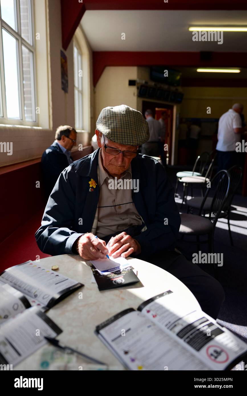 Homme senior portant une casquette plate et écrivant un pari sur un bordereau de pari sur une piste de course hippique, nord de l'Angleterre, Royaume-Uni Banque D'Images