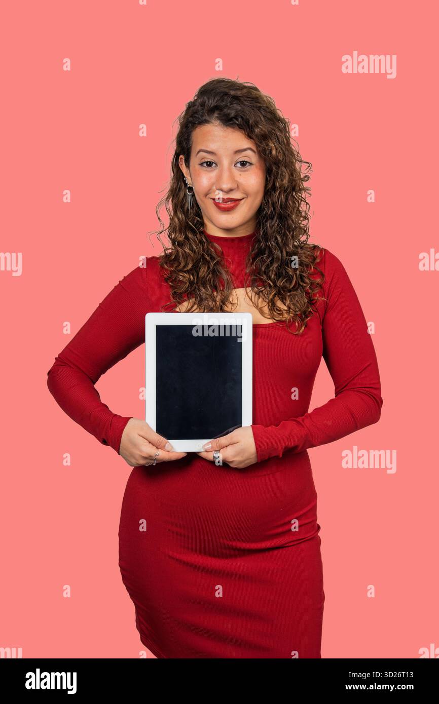 Femme en robe rouge tenant une tablette verticalement avec un écran noir vierge Banque D'Images