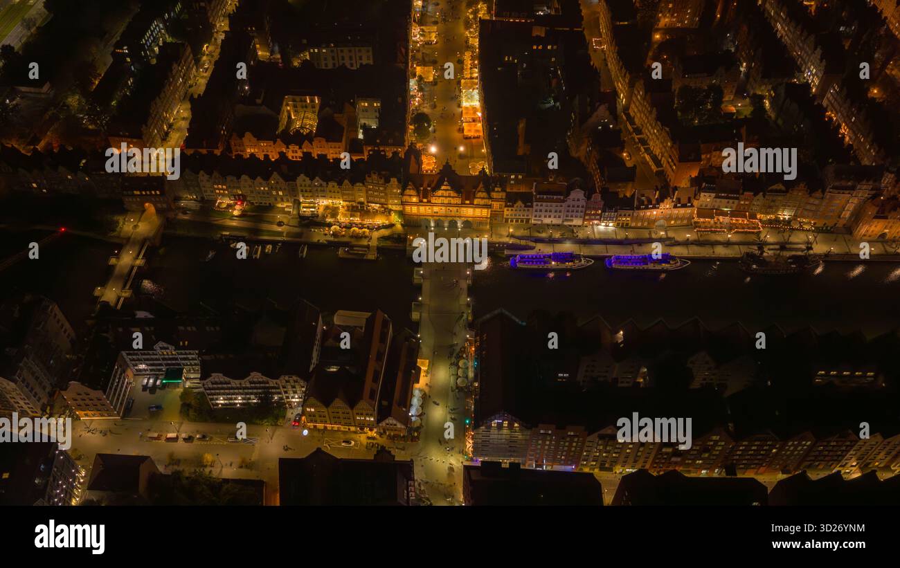 La vue aérienne de nuit de la vieille ville de Gdansk en Pologne montre la rivière Motlawa, la grue Zuraw, long Market et Green Gate, des bateaux d'excursion éclairés bleus et amb chaud Banque D'Images