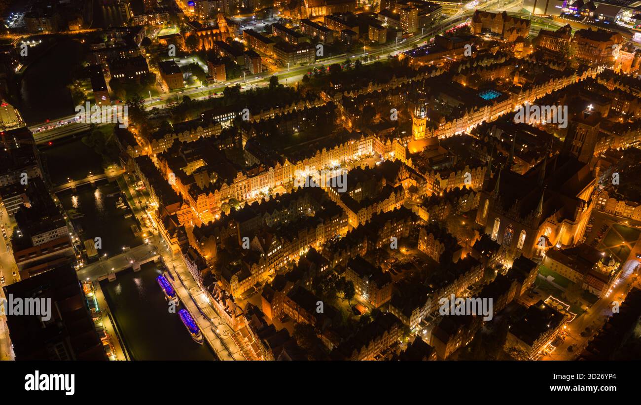 Vue aérienne de nuit montre la vieille ville de Gdansk avec des lumières chaudes, la rivière Motlawa avec des bateaux d'excursion amarrés, l'église de Marys, le Zuraw, et la tour de l'hôtel de ville v Banque D'Images