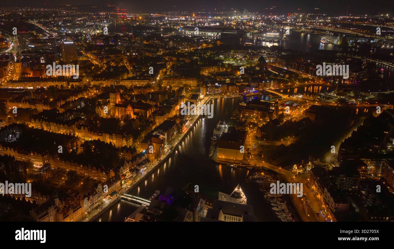 Vue aérienne de nuit de la vieille ville de Gdansk, la rivière Motlawa reflète les ponts et les quais. L’église Marys et la grue de Gdansk se dressent alors que les chantiers navals brillent sur la Pologne Banque D'Images