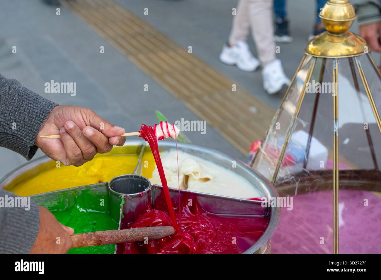 Friandises traditionnelles. Une main enveloppant la taffy colorée et extensible autour d'un bâton. Nourriture de rue, fond bondé. Banque D'Images