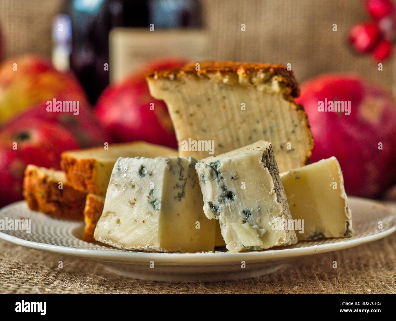 Fromage bleu gorgonzola et fromage poivre jack - Une assiette avec des tranches de fromage gastronomique avec une bouteille de vin et des pommes floues en arrière-plan Banque D'Images