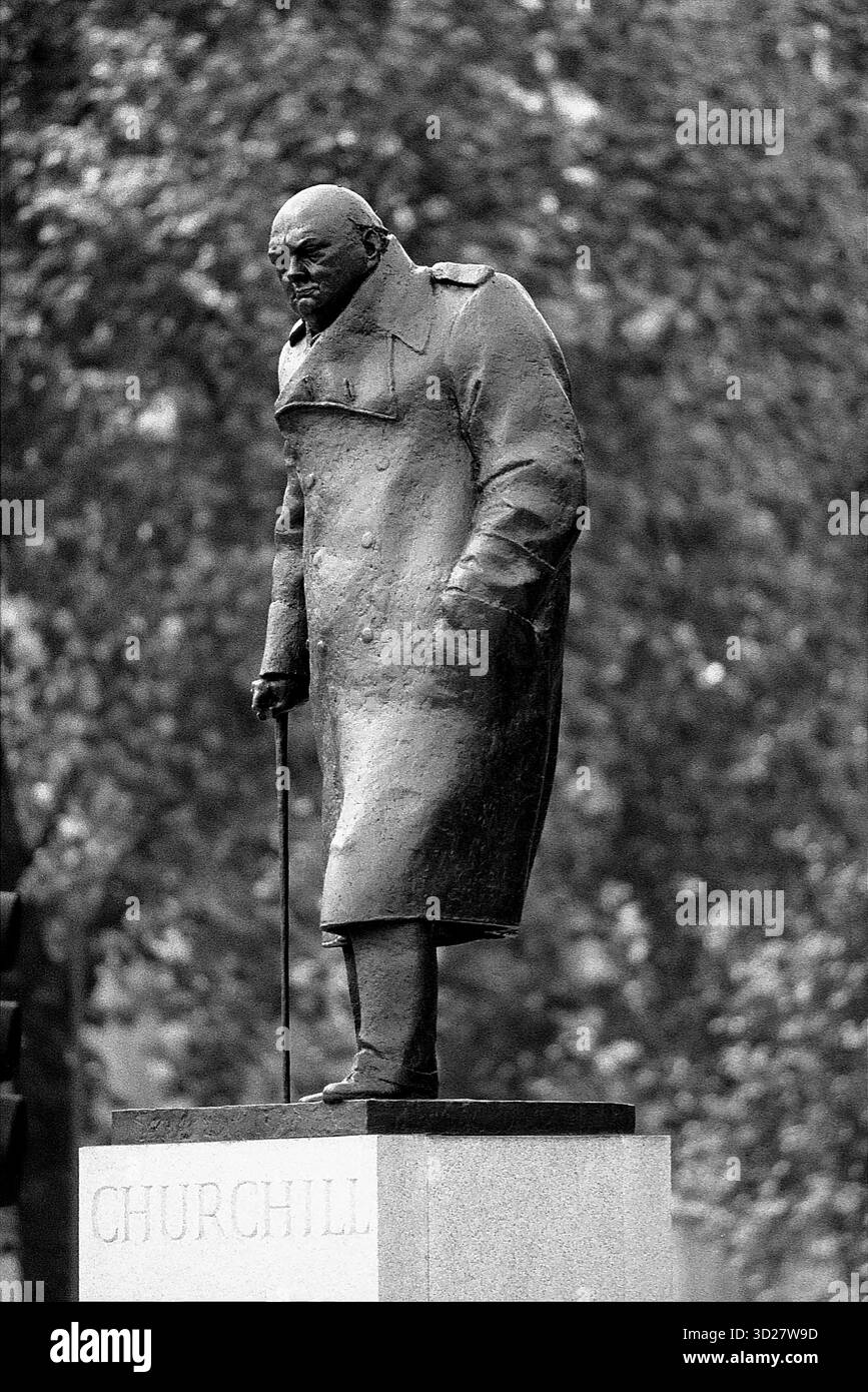 Une image en noir et blanc saisissante capture une statue en bronze de Winston Churchill debout à Londres. La statue, intitulée « Churchill », est placée au milieu d'arbres matures, suggérant un emplacement dans un parc ou un jardin londonien de premier plan. La posture de Churchill, avec sa main posée sur sa canne et son manteau, évoque un sentiment de contemplation et de leadership, une représentation intemporelle de l'emblématique premier ministre britannique. Banque D'Images