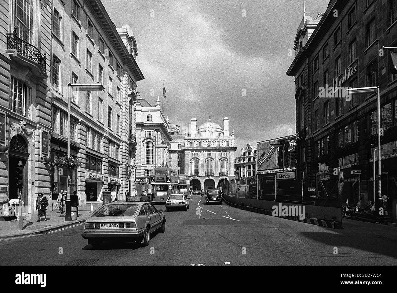 Une scène de rue londonienne classique capture la grandeur de Whitehall, avec le bâtiment emblématique Horse Guards Parade dominant l'horizon. L'architecture imposante et le ciel couvert évoquent un sens de l'histoire et l'énergie animée de la capitale britannique. Banque D'Images