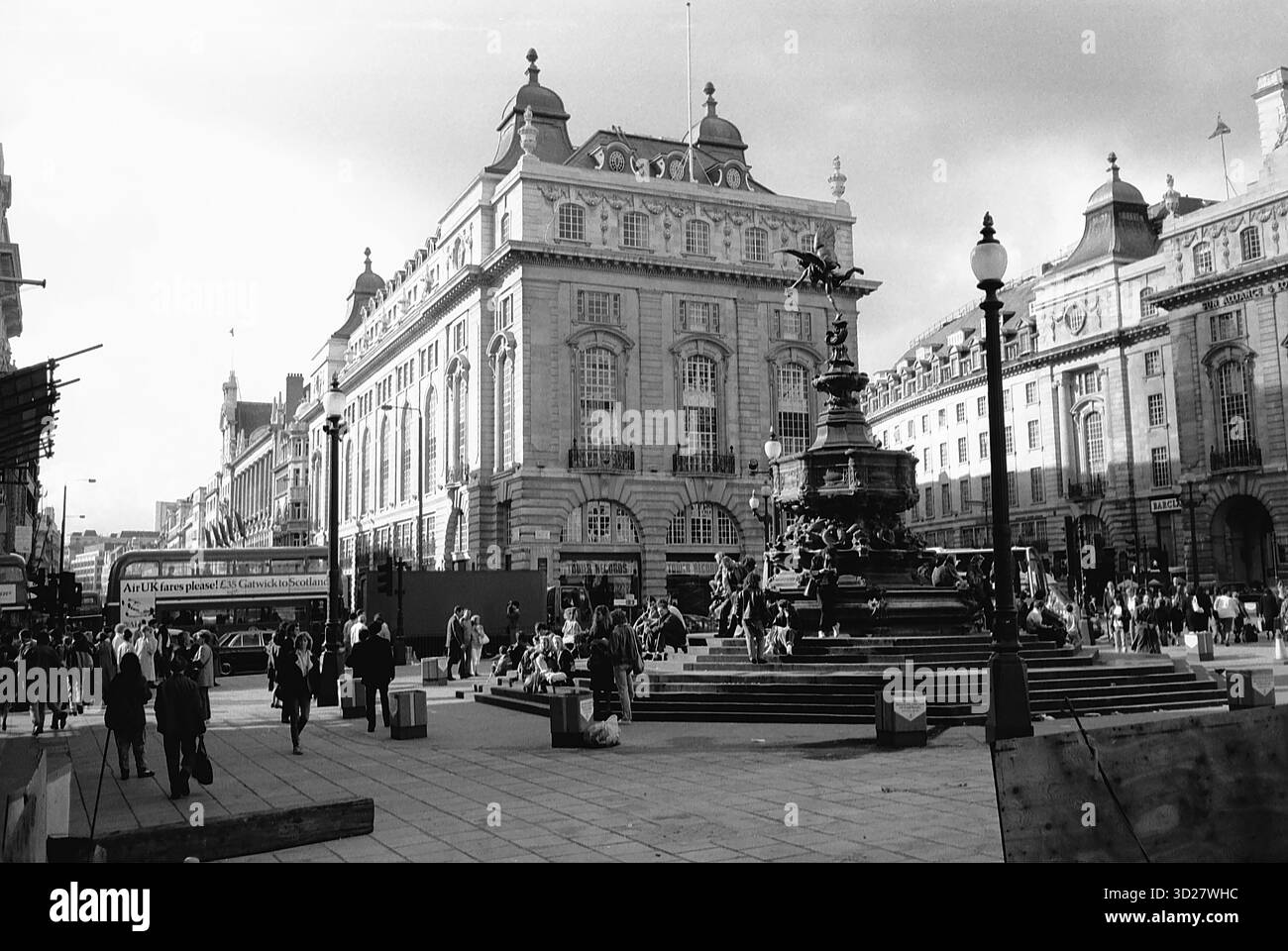 Regent Street, Londres – Une scène intemporelle se déroule sur Regent Street, où la grandeur de l'ancien Lyons Tea Building contraste avec la foule animée en contrebas. La fontaine emblématique, point central de la rue, reflète l'énergie vibrante de cette artère historique de Londres. Acheteurs et touristes se rassemblent autour de la fontaine, capturant un moment au cœur de l'une des destinations shopping les plus prestigieuses de Londres. Banque D'Images