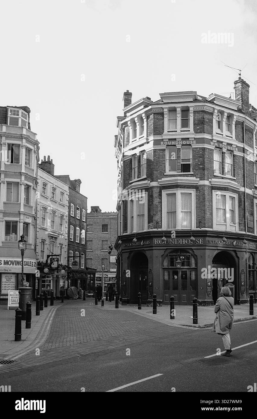 Une scène de rue calme à Bloomsbury, Londres. L'emblématique pub Roundhouse se trouve bien en vue sur la droite, encadré par l'architecture historique de la région. Une figure solitaire descend la rue pavée, ajoutant une touche de solitude à cette vue classique de Londres. Découvrez le charme et l'histoire de Bloomsbury, un quartier imprégné de patrimoine littéraire et artistique. Banque D'Images