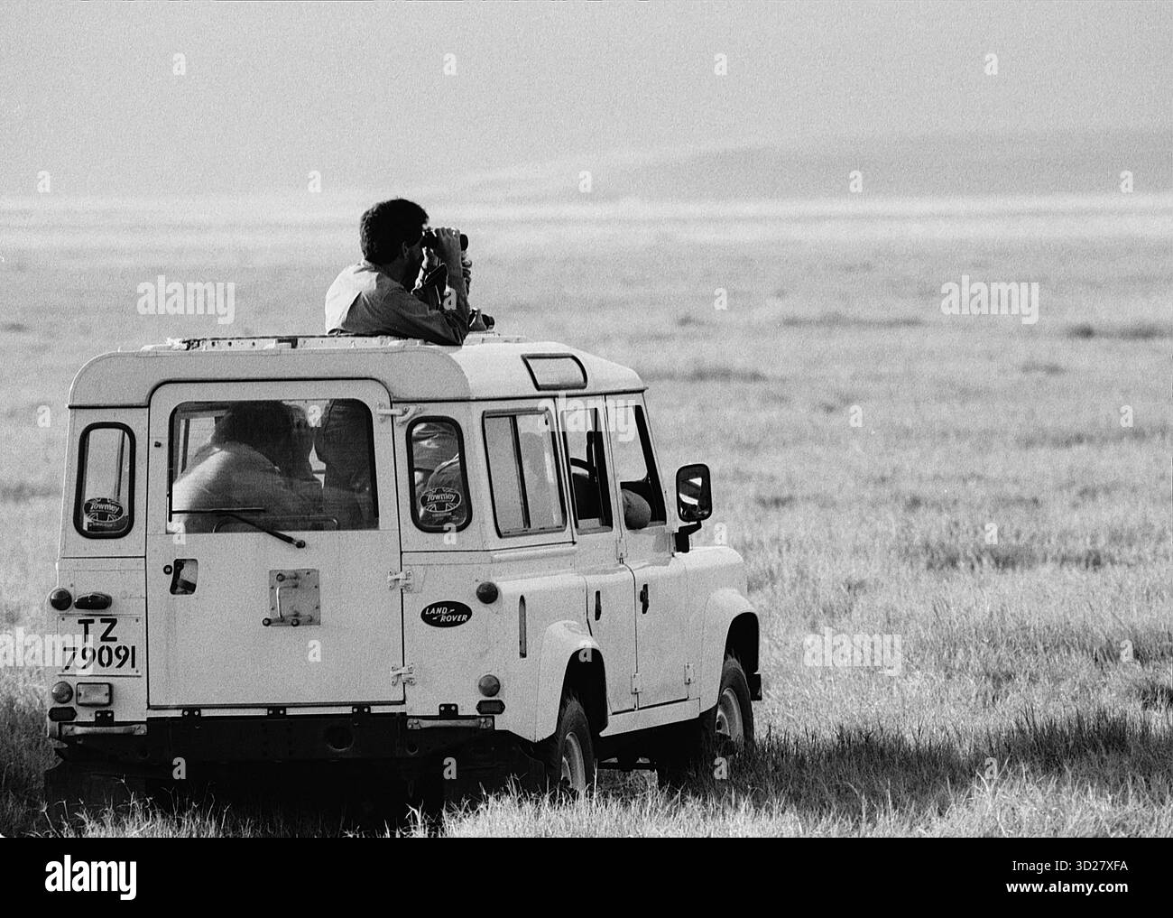 Safari Adventure : un groupe de touristes observe la faune sauvage au sommet d'un Land Rover dans les vastes plaines du parc national du cratère Nagorongoro, en Tanzanie. Ce cratère emblématique, classé au patrimoine mondial de l'UNESCO, possède une formation géologique unique et une faune abondante, offrant aux visiteurs une occasion unique de découvrir la beauté naturelle de l'Afrique. Banque D'Images
