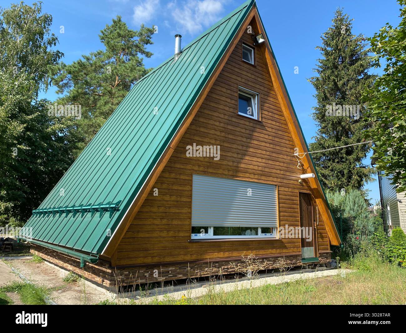 Une cabine moderne et géométrique à cadre En A avec un toit en métal vert abrupt et des stands de parement en bois chauds nichés parmi de grands arbres et de l'herbe verte Banque D'Images