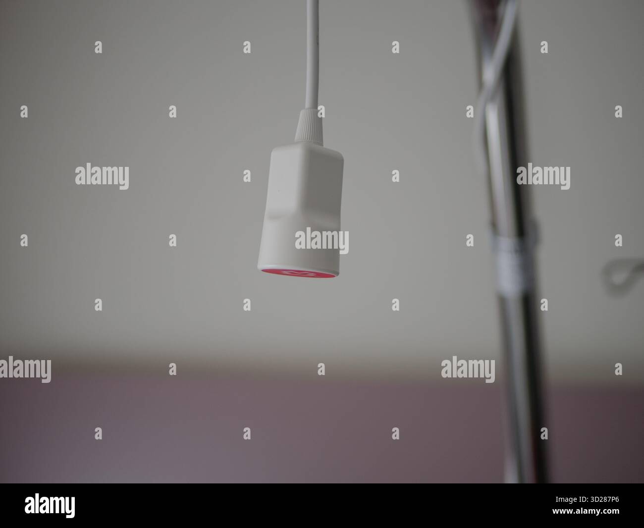 Gros plan d'un bouton d'appel infirmière standard de type pendentif avec boîtier blanc et gâchette rouge, suspendu à son cordon à côté d'une barrière de lit en acier inoxydable Banque D'Images