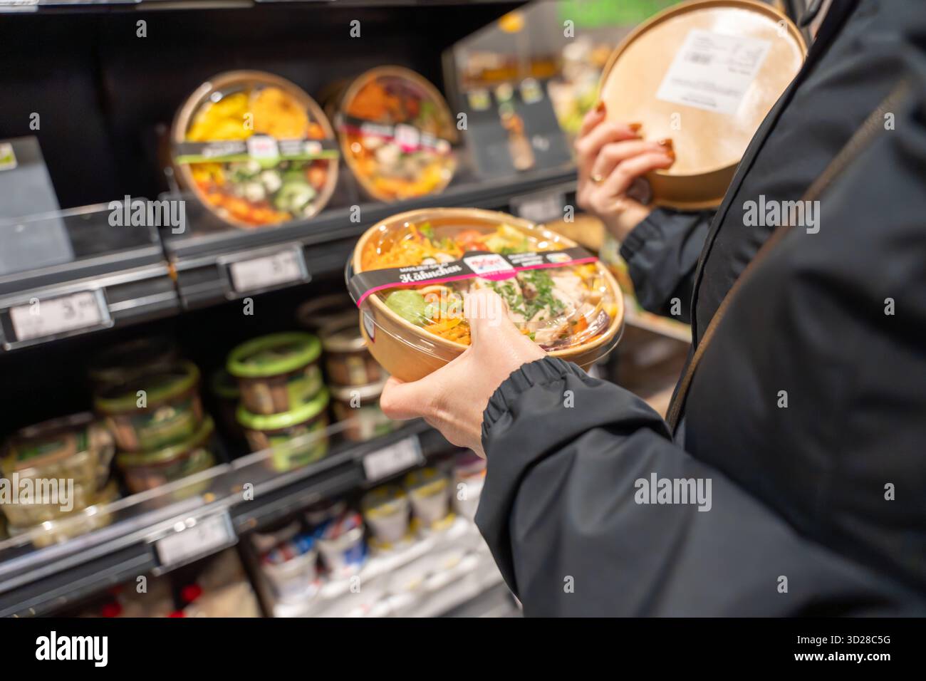 Allemagne Sylt 27.10.2025. Plats cuisinés au supermarché. Un acheteur tient un saladier emballé tout en comparant les produits dans une section réfrigérée. Frais c Banque D'Images
