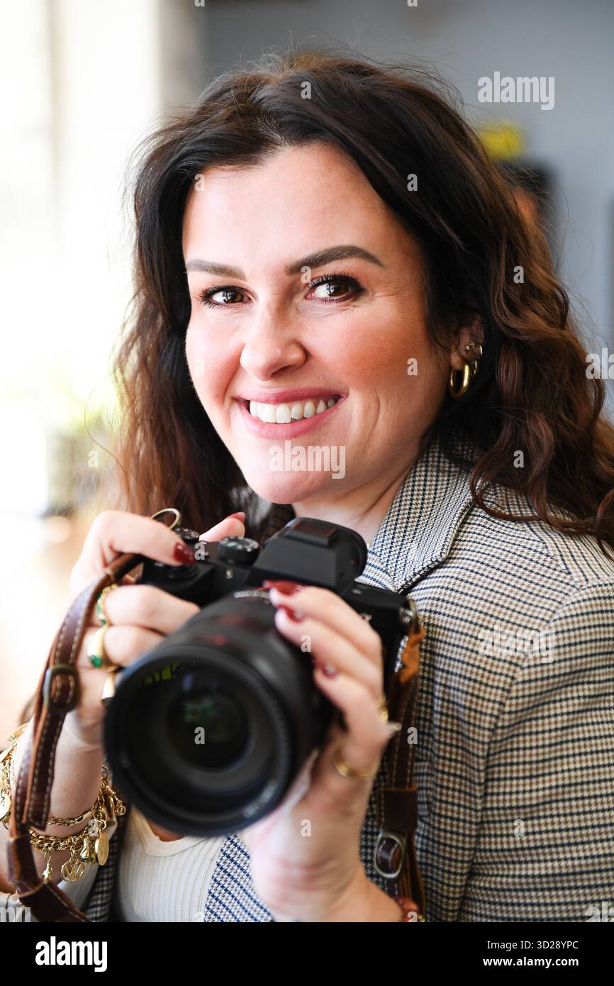 Femme souriante tenant la caméra gros plan dans un blazer avec un bijou en or Banque D'Images