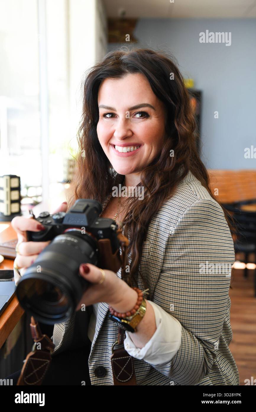 Femme souriante tenant une caméra dans un cadre de café confortable Banque D'Images
