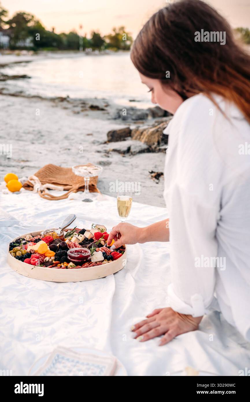 Femme aime pique-niquer charcuterie près de la plage au coucher du soleil Banque D'Images