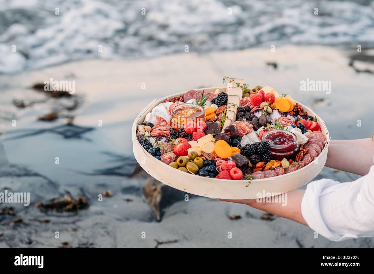 Planche de charcuterie tenue près de la marée océanique au rivage. Banque D'Images