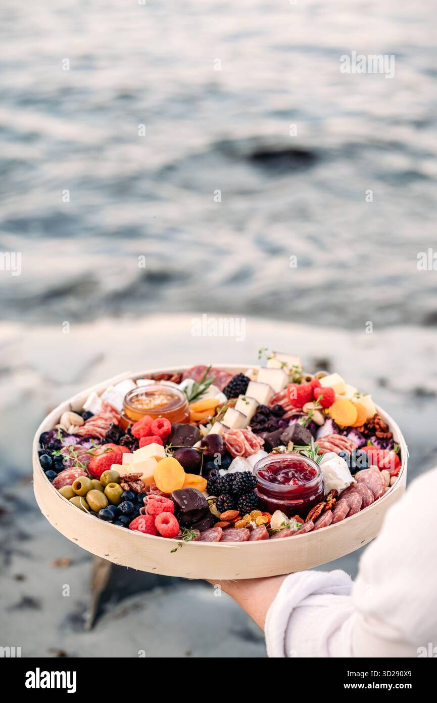 Planche de charcuterie tenue près de la marée océanique au rivage. Banque D'Images