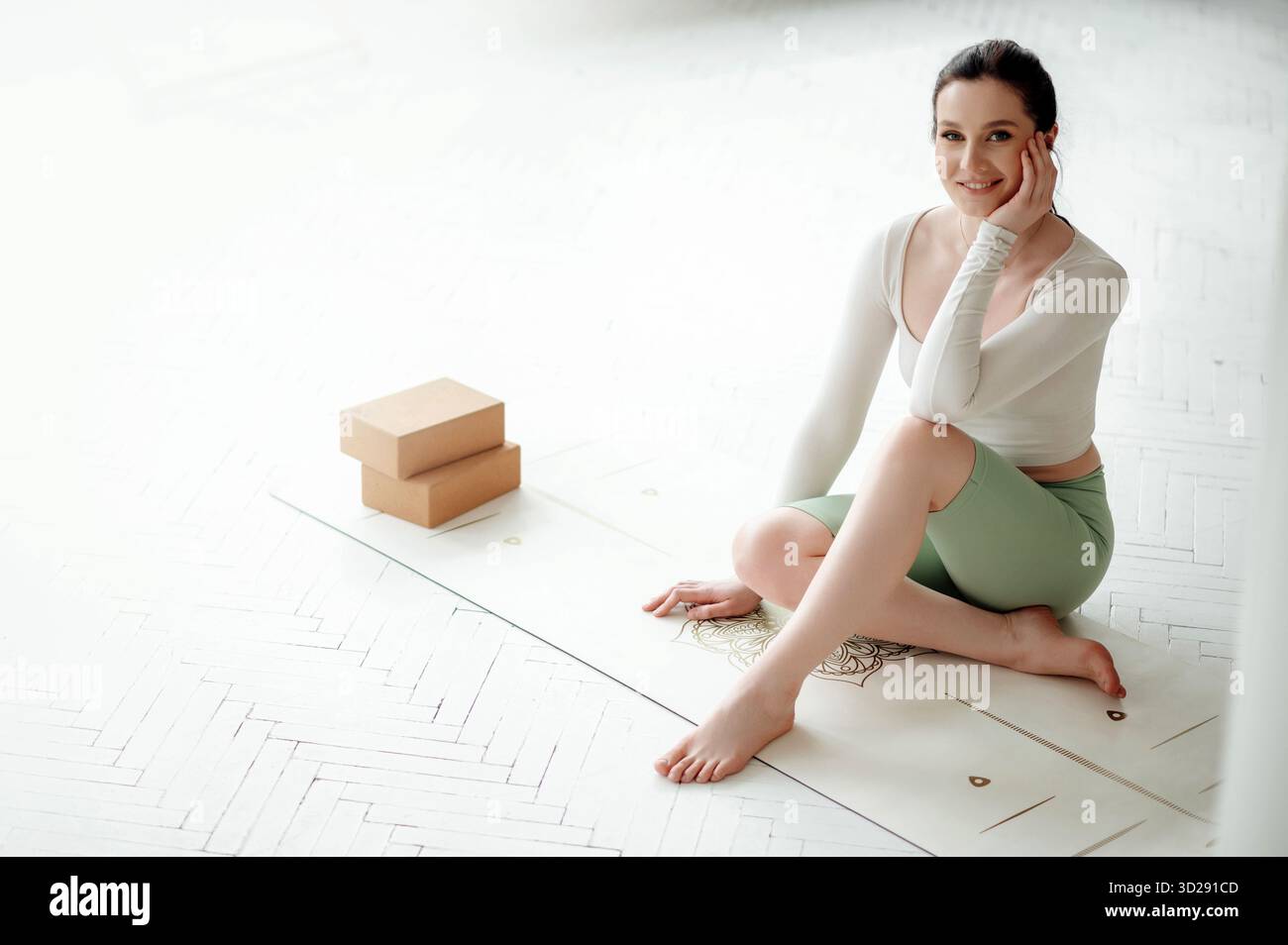 Femme en chemise blanche assise sur le mat de yoga et souriant à la caméra Banque D'Images