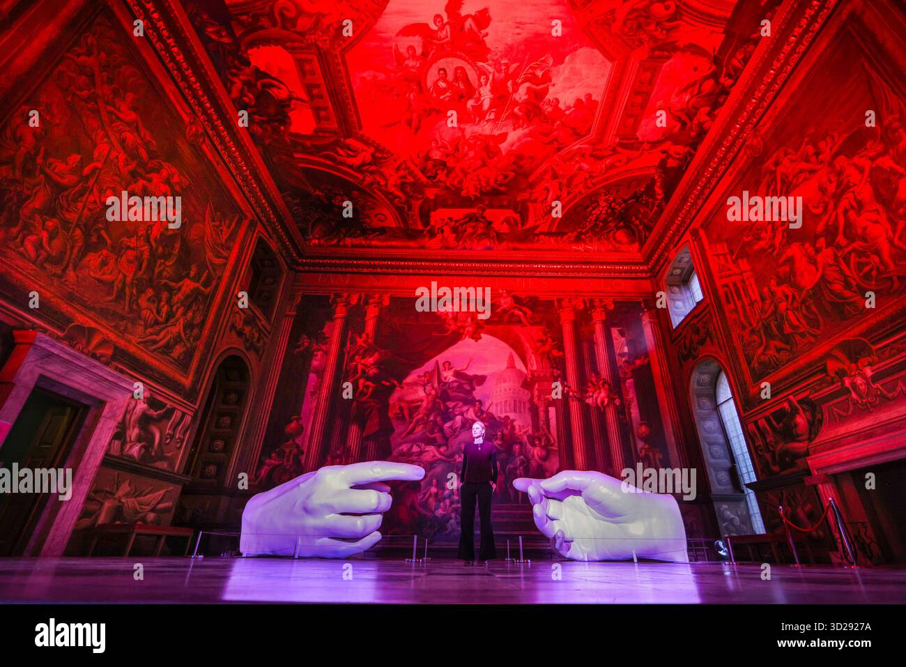 Londres, Royaume-Uni. 31 octobre 2025. Personnel avec les installations de Peter Walker 'Connection' and Identity' dans le Painted Hall de l'Old Royal Naval College, Greenwich. « Identity » montre huit colonnes suspendues illuminées, évoquant les structures de l'ADN, et « Connection » est une réinterprétation moderne de la création d'Adam de Michel-Ange, remplaçant les mains traditionnellement masculines par des moulages de mains féminines. Crédit : Imageplotter/Alamy Live News Banque D'Images