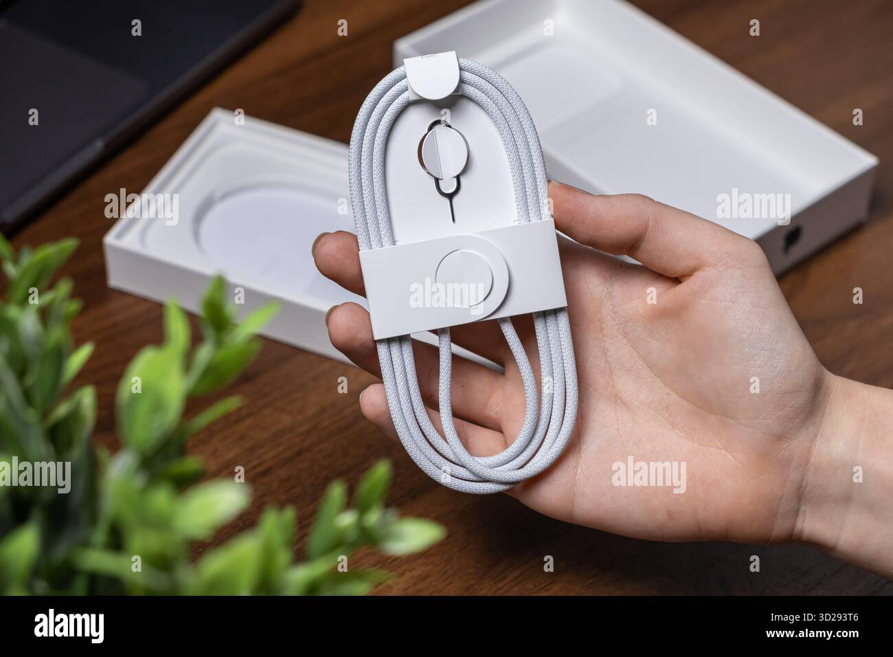 Poznan, Pologne - 16 octobre 2025 : présentation manuelle du nouveau câble de chargement USB tressé blanc enroulé et de l'outil d'éjection SIM, accessoires numériques cruciaux pour M. Banque D'Images