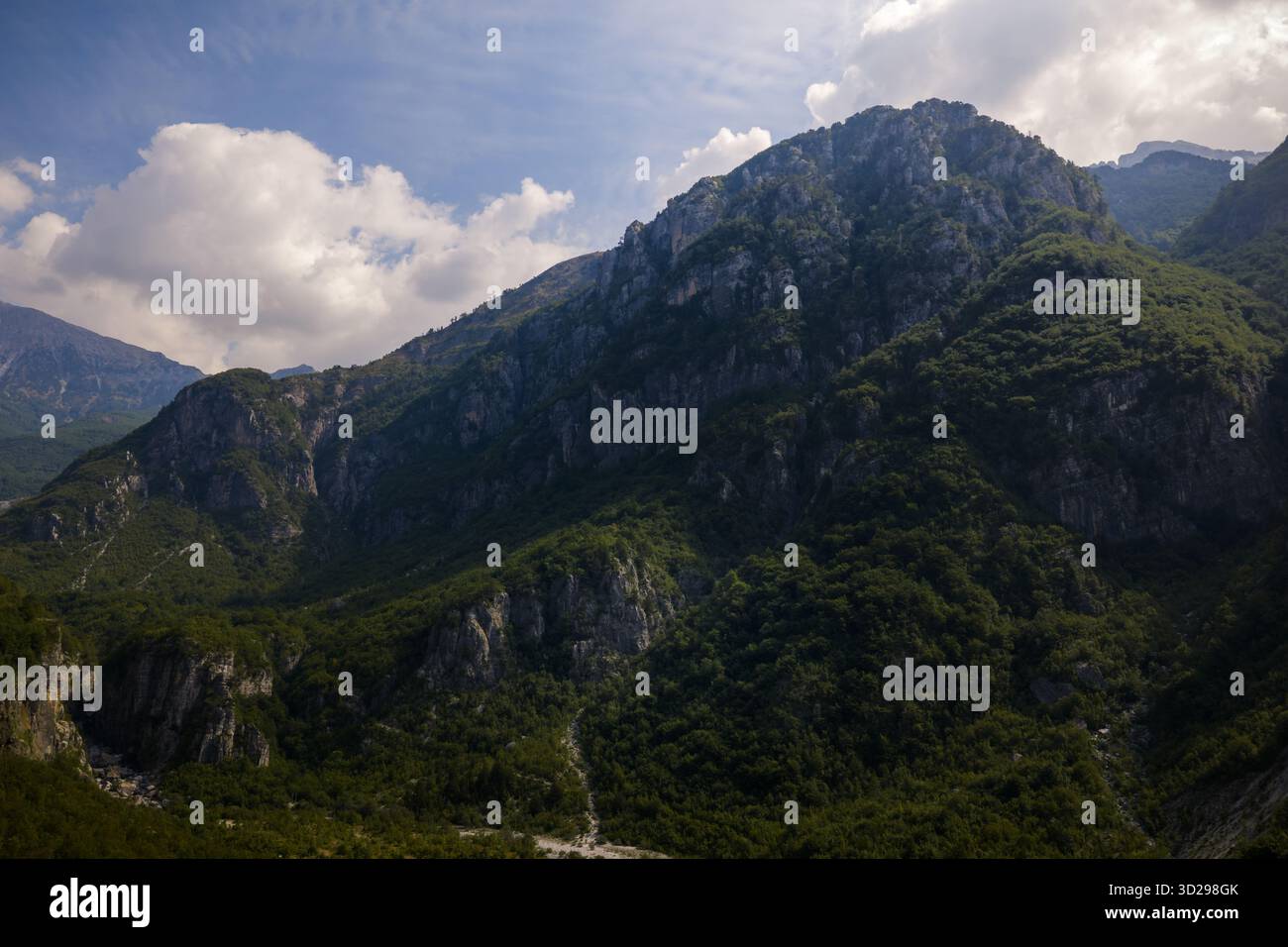 Vue aérienne des montagnes escarpées recouvertes de forêts verdoyantes, montez vers un ciel parsemé de nuages blancs et moelleux, créant un contraste fascinant de te Banque D'Images