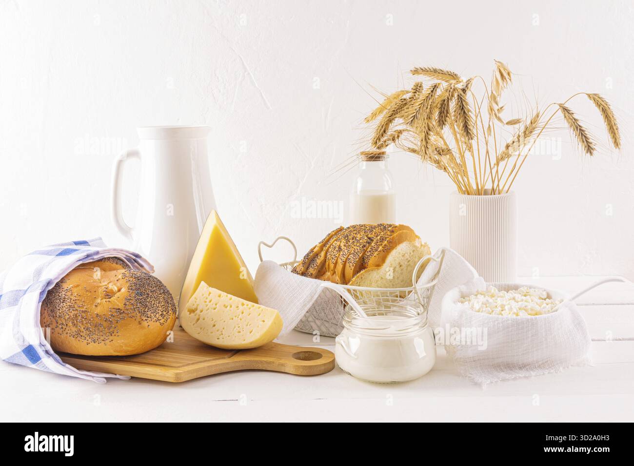 De nombreuses variétés de fromage sur une planche, des bouteilles de lait, du fromage cottage, de la crème sure, un bouquet d'épis de pain sur une table en bois. La fête de Shavuot Banque D'Images