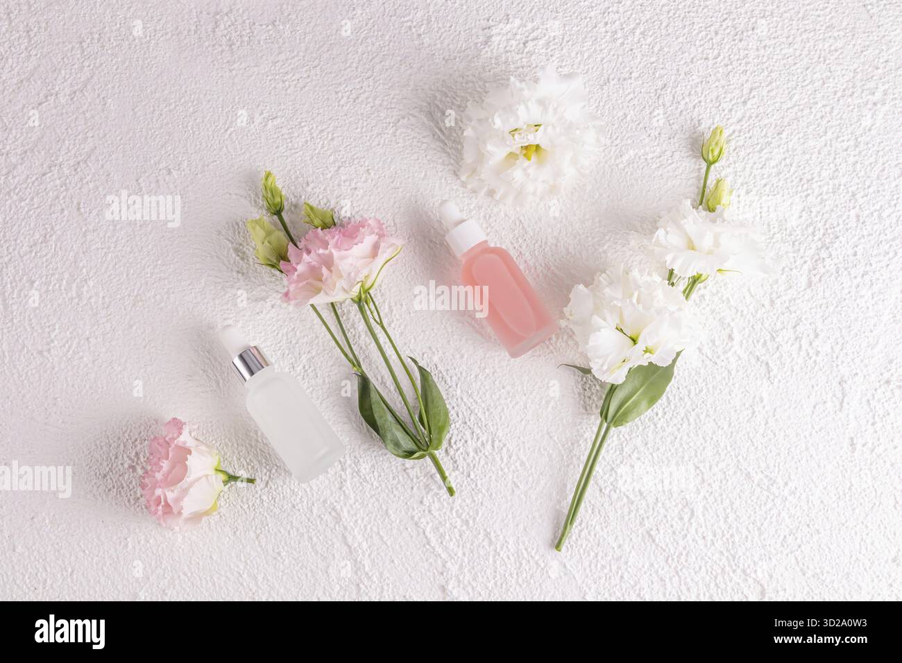 Deux bouteilles cosmétiques mates avec un compte-gouttes avec un produit de soins de la peau naturel pour le visage sur un fond blanc parmi les fleurs printanières délicates. Pose à plat Banque D'Images