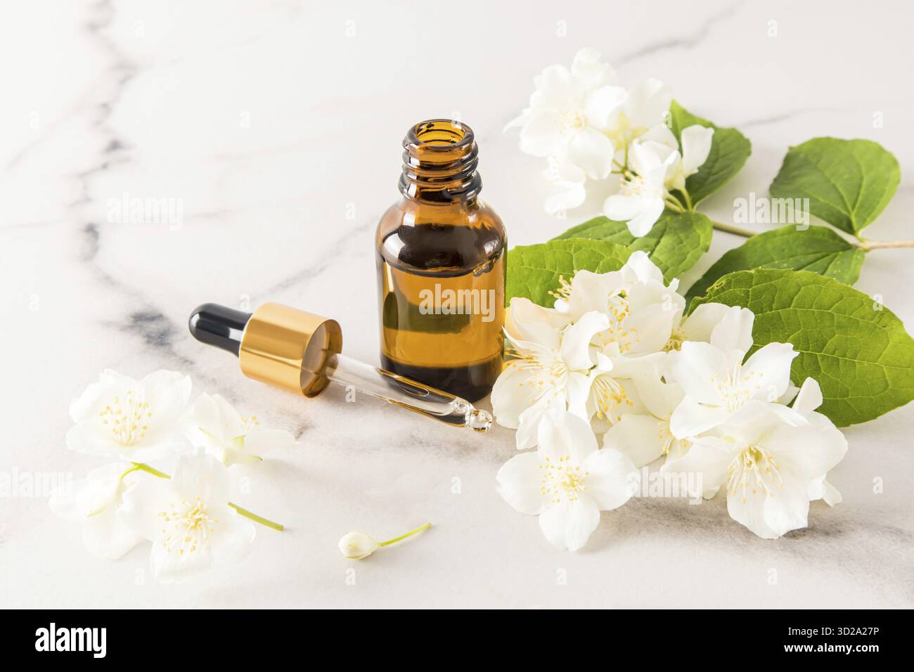 Une bouteille ouverte d'huile de jasmin et un compte-gouttes avec un produit cosmétique sur fond de fleurs de jasmin parfumées. le concept d'autosoins Banque D'Images