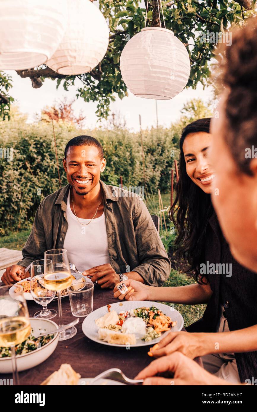 Homme souriant mangeant de la nourriture tout en profitant avec des amis de la famille au dîner dans la cour arrière Banque D'Images