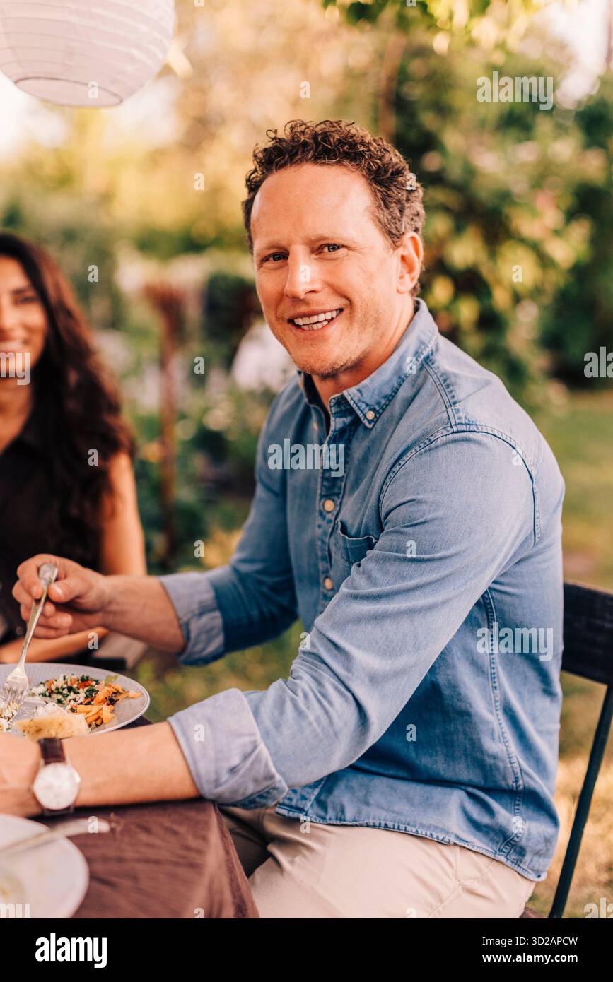 Portrait d'homme heureux mangeant de la nourriture tout en étant assis à la table à manger dans la cour arrière Banque D'Images