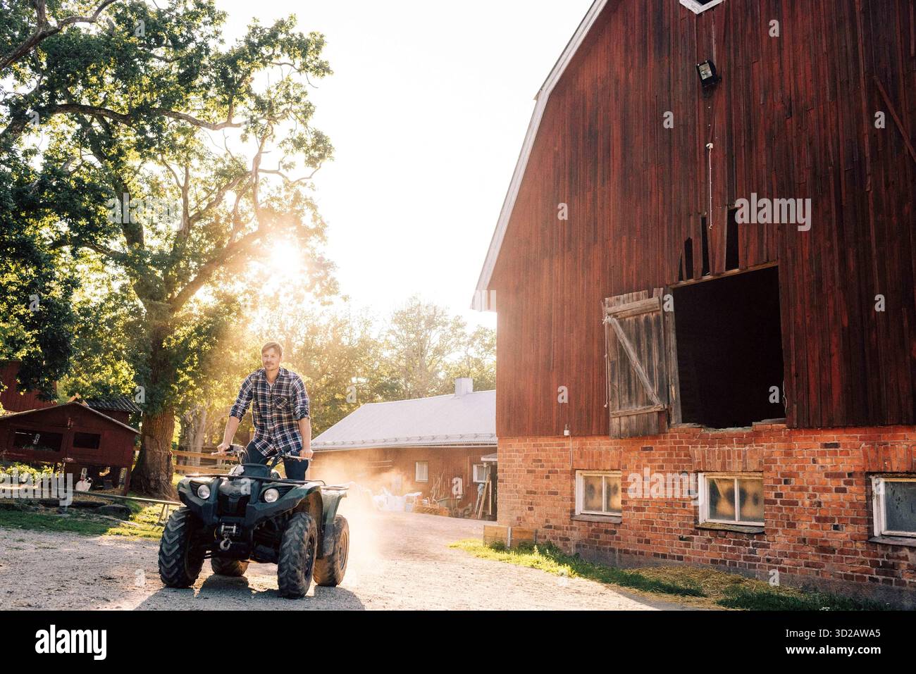 Agriculteur conduisant quadbike à la ferme pendant la journée ensoleillée Banque D'Images