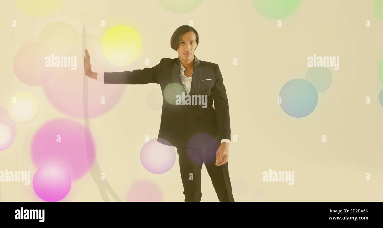 Posant le modèle asiatique prolongeant le bras gauche sur le panneau vertical blanc dans le studio crème, avec des cercles pastel Banque D'Images