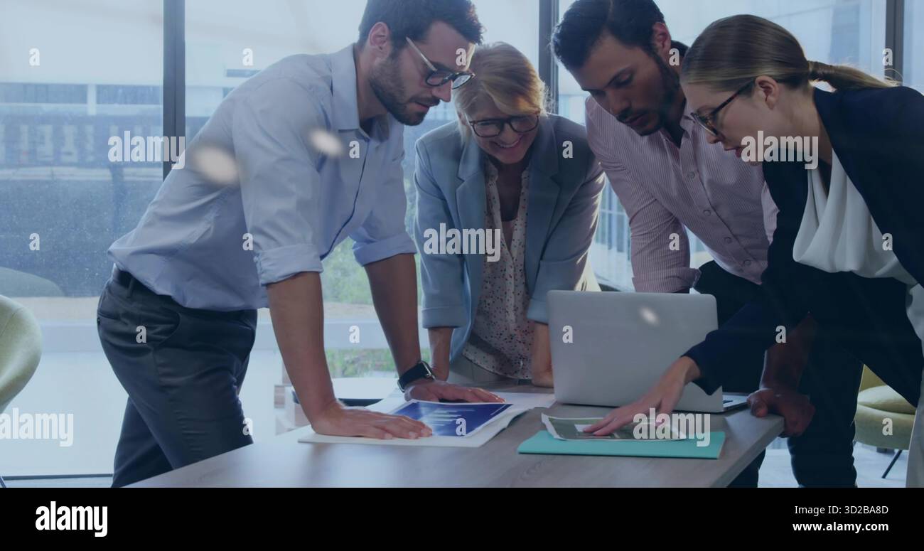 Collaborateurs se penchant autour d'une table de réunion au bureau avec ordinateur portable et graphiques imprimés Banque D'Images