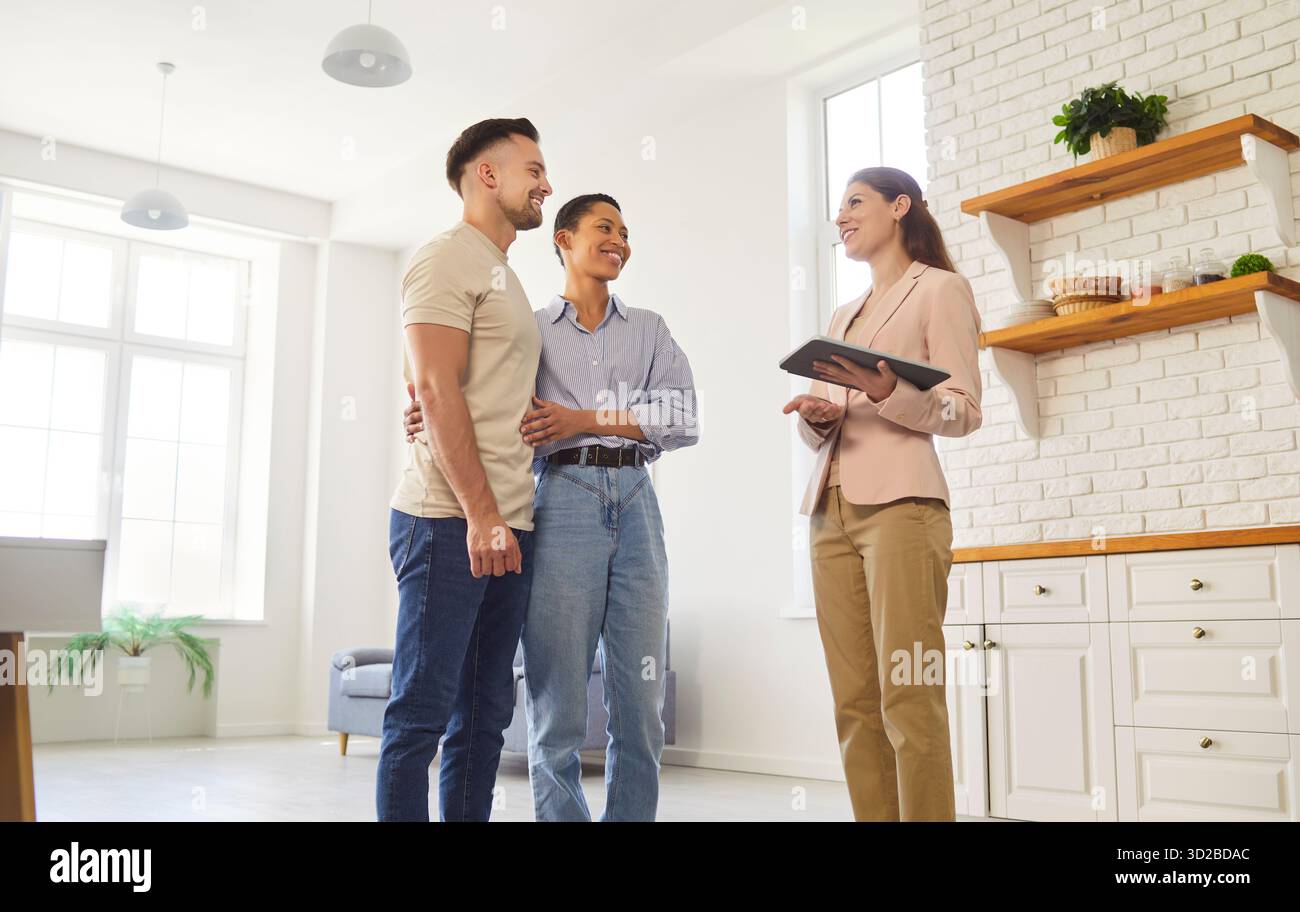 Agent immobilier et jeune couple marié debout dans la cuisine domestique moderne Banque D'Images