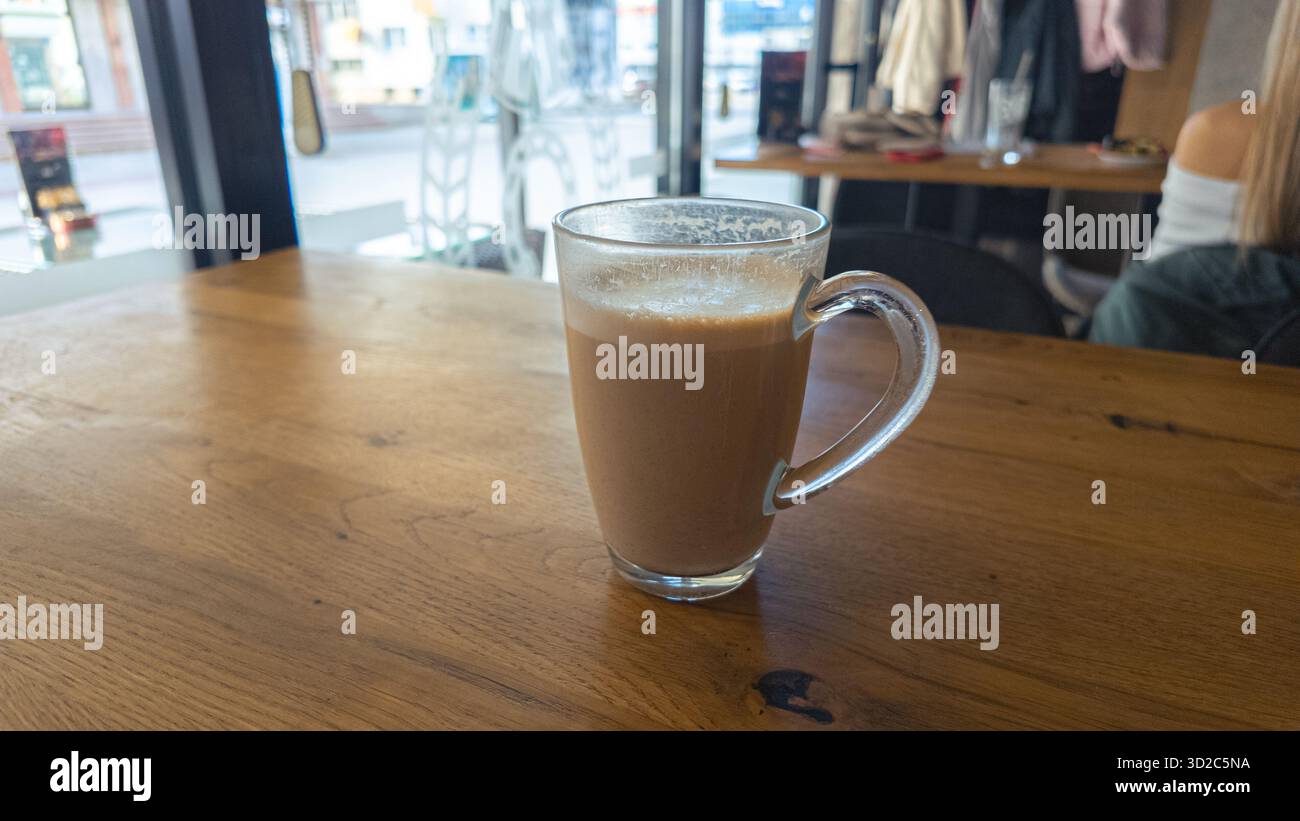 Café chaud dans une tasse en verre sur une table en bois près de la fenêtre lumineuse à l'intérieur du café, atmosphère moderne idéale pour les concepts de style de vie et de relaxation. Banque D'Images