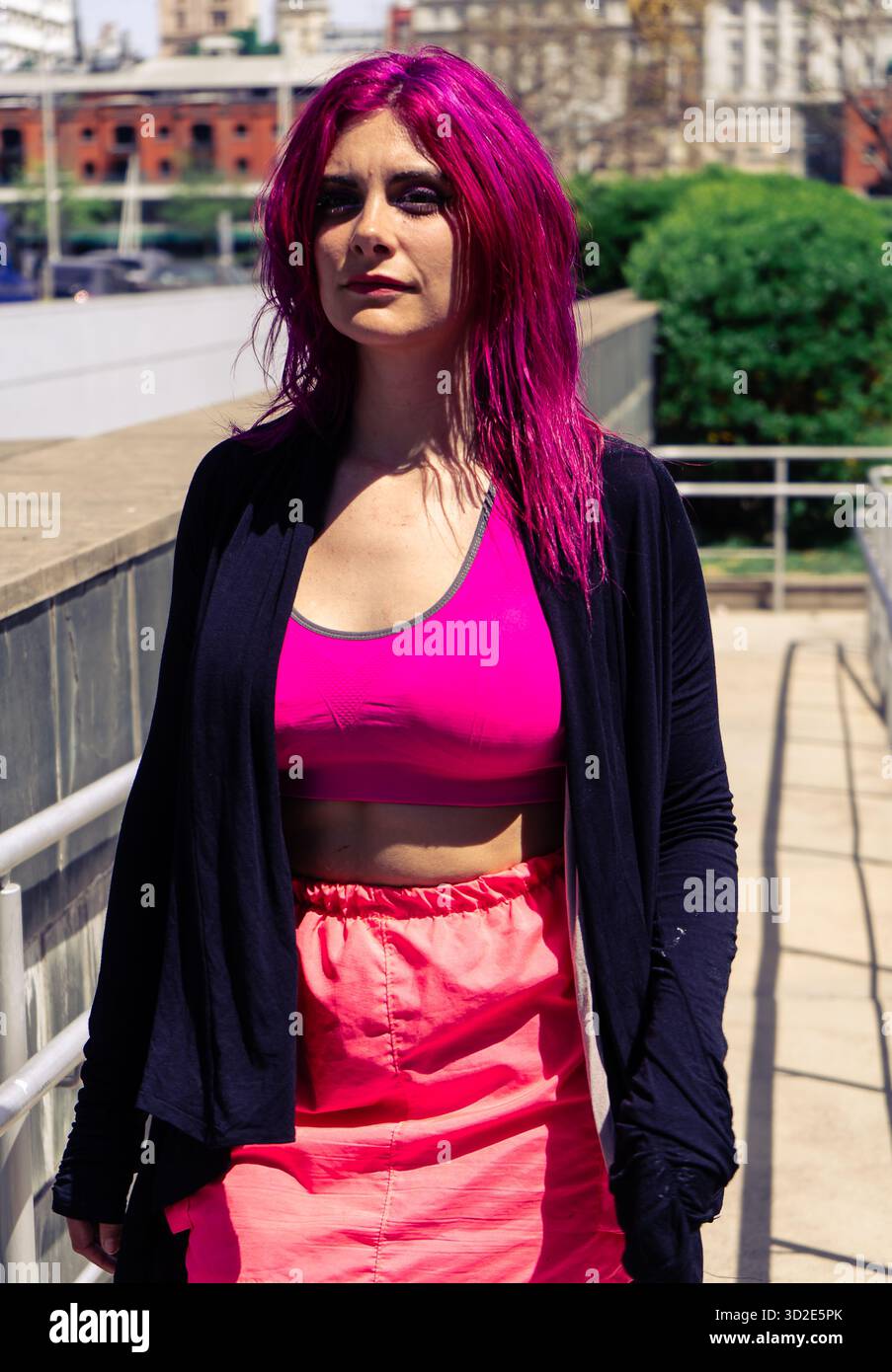 Femme avec des cheveux roses vibrants et un style de mode alternatif posant en toute confiance dans un environnement urbain Banque D'Images