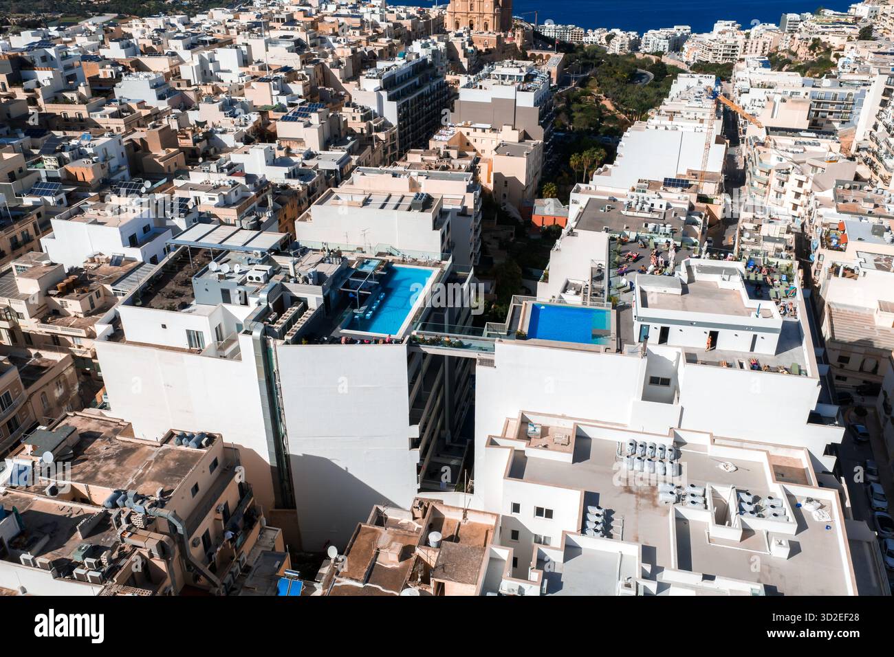 La vue aérienne de Mellieha, Malte montre des toits plats remplis, deux piscines à débordement sur le toit, le dôme de l'église paroissiale et des tours jumelles, la mer bleue au-delà, le midi croustillant Banque D'Images