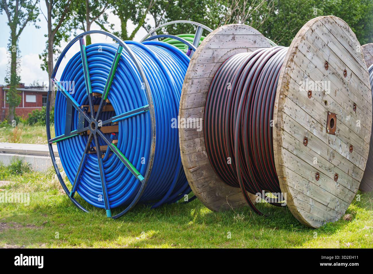 wo grandes bobines avec des câbles enroulés bleus et noirs debout sur l'herbe, préparés pour l'infrastructure installation d'électricité souterraine, énergie infrastru Banque D'Images