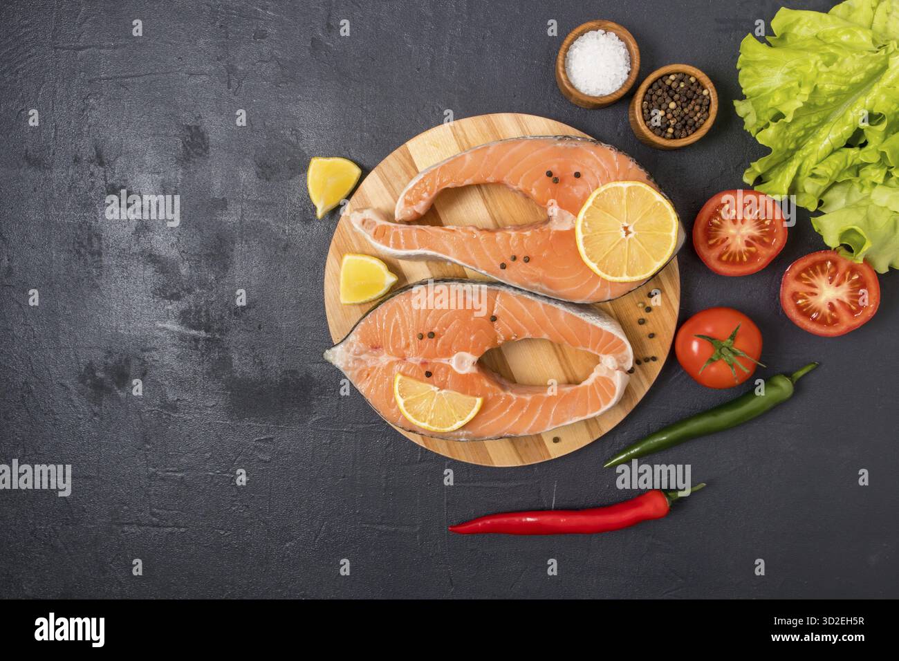 Deux steaks de saumon crus sur une planche de cuisine ronde avec des ingrédients pour la cuisson. source d'oméga 3 et de graisses saturées. vue de dessus. fond noir Banque D'Images