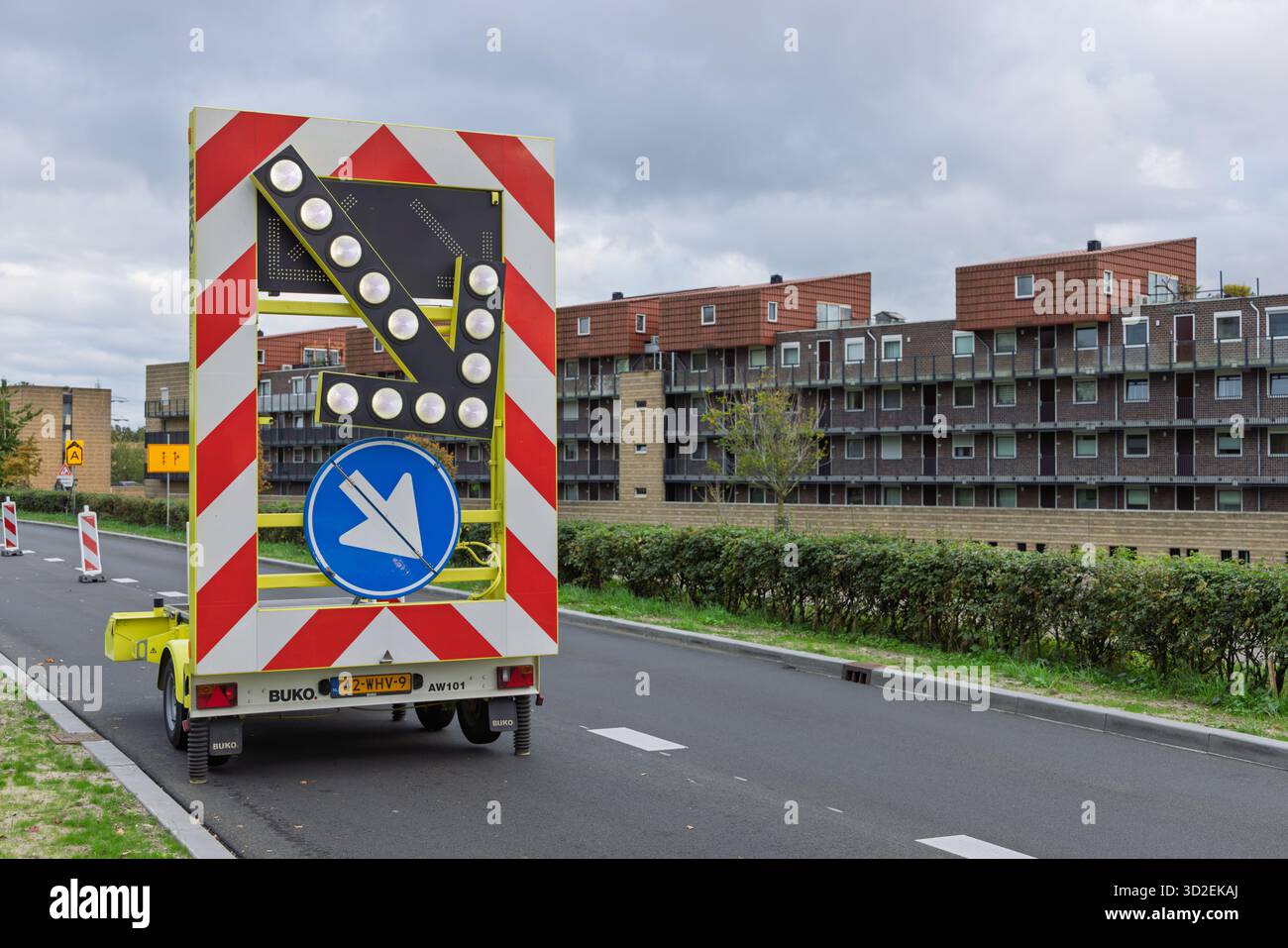 Une remorque de panneau de flèche jaune dans une rue aux pays-Bas, affichant une flèche vers le bas à droite pour détourner la circulation près des immeubles d'habitation modernes. Banque D'Images